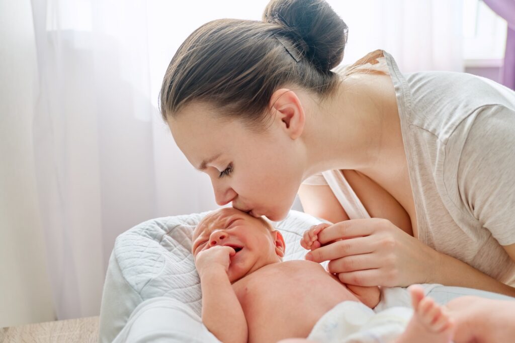 Young mom kissing crying newborn baby son