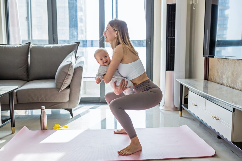 Young Mother Exercising at Home With Baby. Online Training During Coronavirus Quarantine